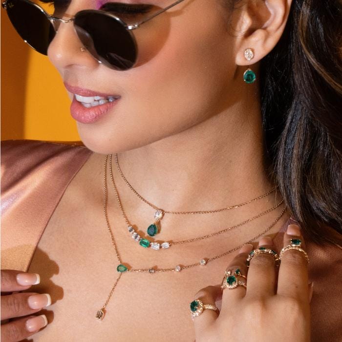 A stylish woman wearing necklaces studded with diamond and green gemstones with matching rings and earrings.